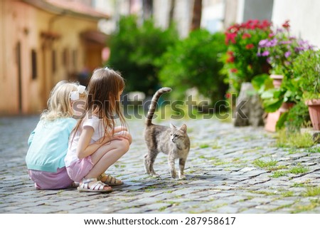 Two adorable little sisters met a cat while walking narrow streets ot typical italian town