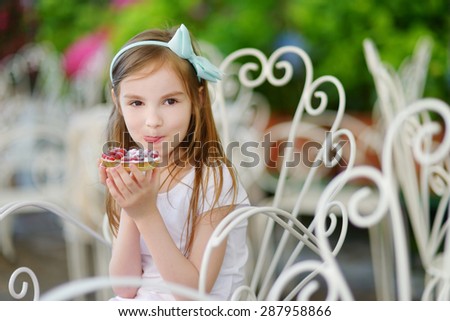 Adorable little girl eating fresh sweet strawberry cake outdoors on warm and sunny summer day in Italy