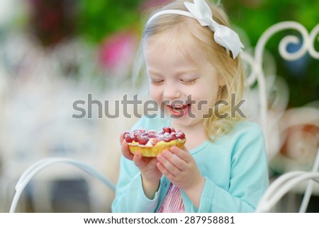 Adorable little girl eating fresh sweet strawberry cake outdoors on warm and sunny summer day in Italy