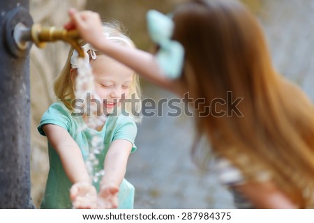 Two sisters having fun with drinking water fountain in Italy on warm and sunny summer day