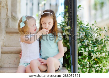 Two adorable little sisters laughing and hugging on warm and sunny summer day in italian town