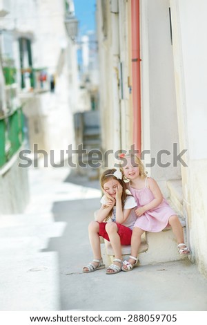 Two adorable little sisters laughing and hugging on warm and sunny summer day in Vieste, Italy