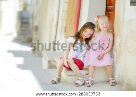 Two adorable little sisters laughing and hugging on warm and sunny summer day in Vieste, Italy