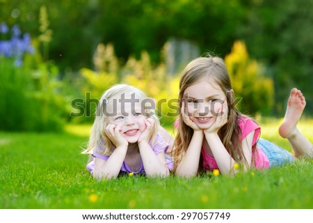 Two cute little sisters having fun while laying on the grass on a sunny summer day