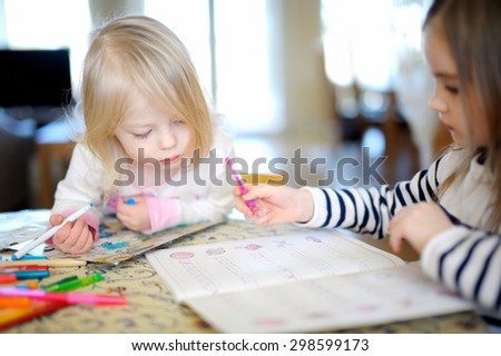 Two little sisters drawing and learning together at home