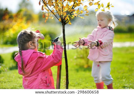 Two adorable little mommy\'s helpers watering plants in the garden on beautiful autumn day