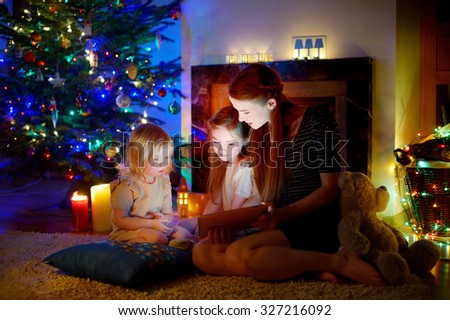 Young mother and her daughters using a tablet pc by a fireplace on warm Christmas evening