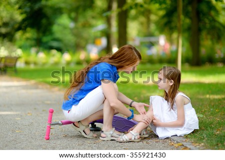Mother comforting her daughter after she fell while riding her scooter at summer park