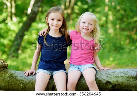 Two adorable little sisters hiking in a forest on warm and sunny summer day