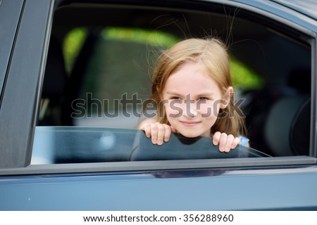 A little girl is sticking her head out the car window looking forward for a roadtrip or travel
