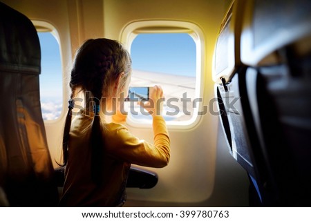 Adorable little girl traveling by an airplane. Child sitting by aircraft window and looking outside.