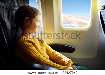 Adorable little girl traveling by an airplane. Child sitting by aircraft window and looking outside.