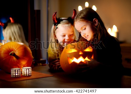 Two pretty young sisters in halloween costumes carving a pumpkin together on Halloween