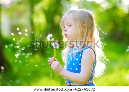 Pretty little blonde girl blowing off a dandelion on beautiful sunny summer day