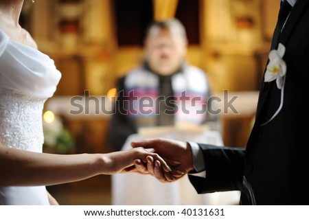 Bride and groom are holding each other\'s hands during church wedding ceremony
