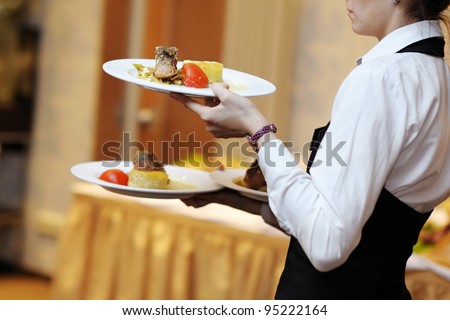 Waitress is carrying three plates with meat dish
