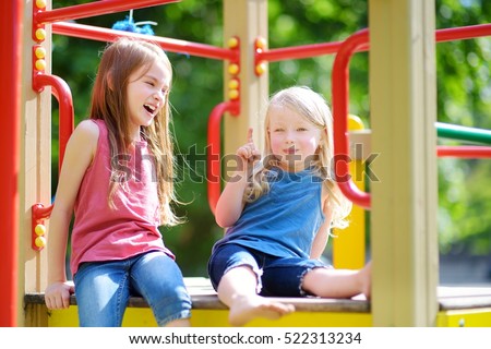 Two cute little girls having fun on a playground outdoors in summer