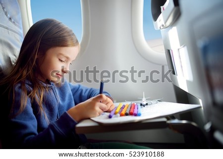 Adorable little girl traveling by an airplane. Child sitting by aircraft window and drawing a picture with colorful pencils.