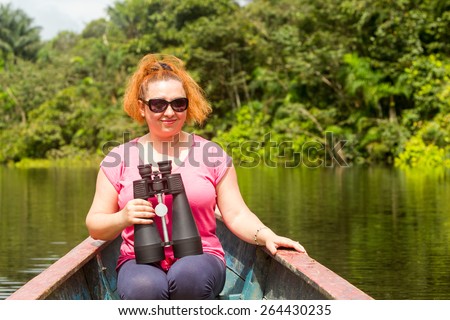 Tourist woman with high power binoculars in Amazonian jungle against dense vegetation