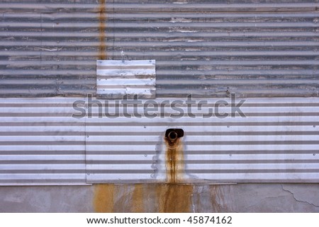 Metal wall texture with drain and rusty water stains.