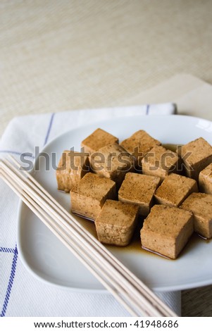 Close up of marinated tofu on a white plate with wooden skewers and a dishcloth.