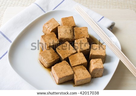 Close up of marinated tofu on a white plate with wooden skewers and a dishcloth.