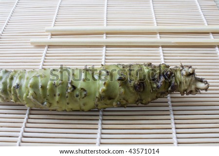 Selective focus image of fresh wasabi root also called Japanese horseradish on a bamboo mat with chopsticks.
