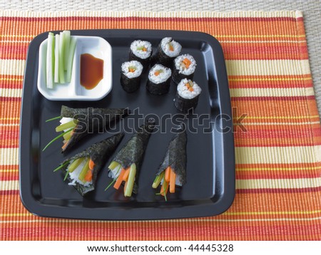 Bird\'s eye view of a plate with different kind of sushi, like maki and temaki with orange striped background.