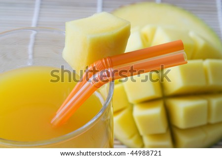 Selective focus image of a mango juice with orange straw and mango in the background.