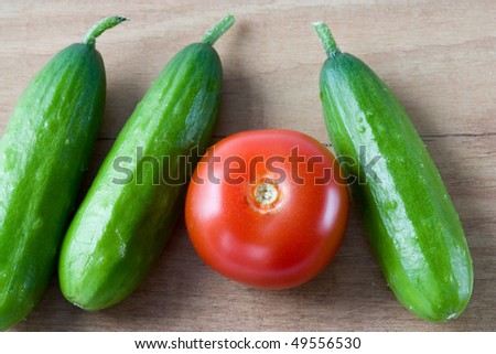 Selective image of small English cucumber with a tomato on a wooden countertop