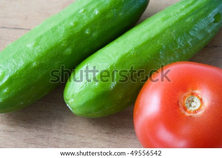 Selective image of small English cucumber with a tomato on a wooden countertop