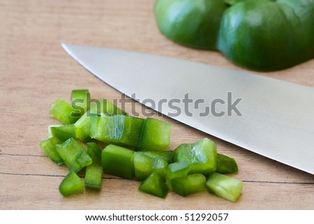 Selective focus image of chopped green pepper and a knife on a wooden board.