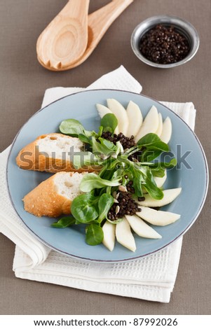 Field Salad with pears, flatbread and black lentils, served on a blue colored plate.