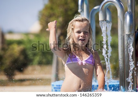A little girl playing with water in a fountain having a swim