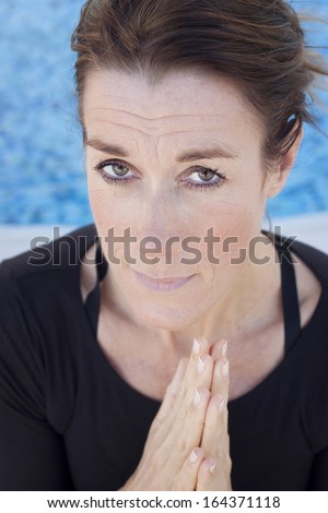 A middle aged smiling lady doing a yoga greeting, namaste, looking at camera, wrinkles, mindfulness