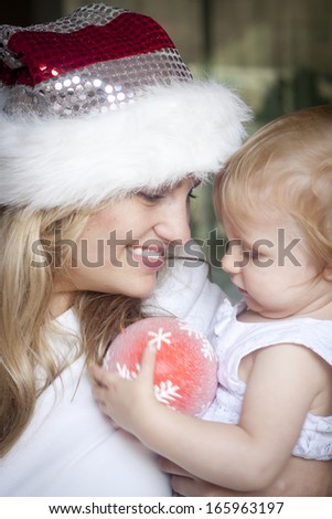 A smiling mum holding a cute toddler with a christmas decoration. Slight blur in photo
