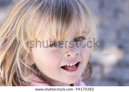 Closeup of a beautiful little girl with sparkling eyes and a cheeky smile. Background out of focus. Positive, happy feeling
