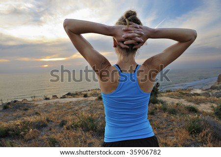 Woman runner stretches at the end of a run, sunset in background