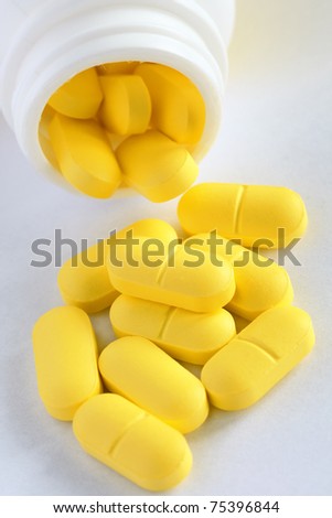 close-up full bottle of yellow pills and heap near it