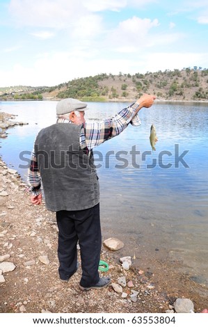 A senior fisherman just caught a fish by lake/sea