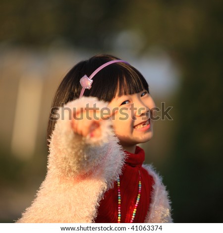 A little Chinese girl standing and with one arm outstretched is pointing her finger