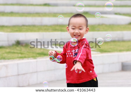 The happy asian Chinese boy in red is playing the soapbubble.