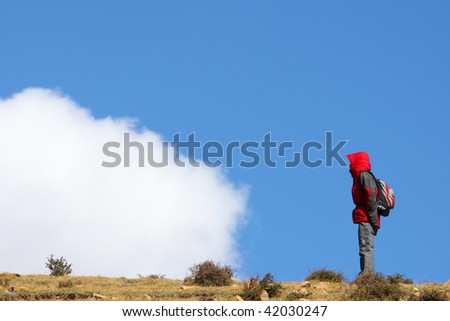 A lady in red is standing on the top of the mountain facing to the clouds.