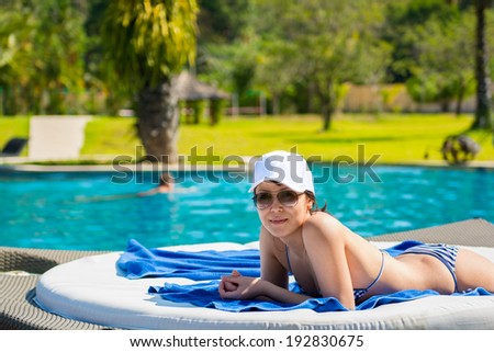 Portrait of a young beautiful woman in white cap and sunglasses lying on a sun lounger on against the background of the pool background. The concept of leisure and tourism