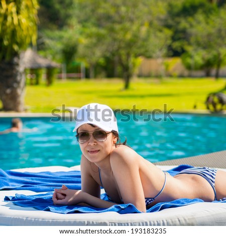 Portrait of a young beautiful woman in white cap and sunglasses lying on a sun lounger on against the background of the pool background. The concept of leisure and tourism
