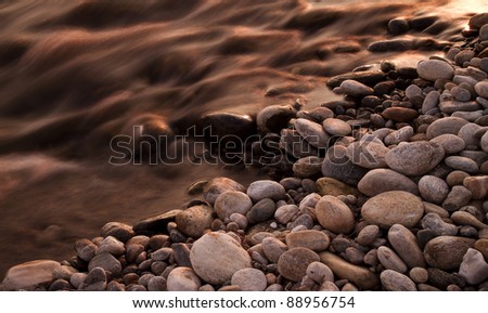 A serenity-inspiring image of a river flowing near a bed of rocks illuminated by the warm sunset light