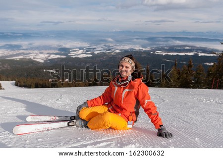 Young skier woman in orange suit resting on snow hill