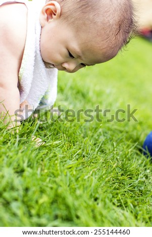 One happy baby sits on the grass in park, her hands on grass and looks at the grass