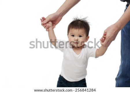 A baby girl is learning walking with the help of her parent, looking at the camera and smiling, isolated on white background