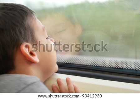 A happy child boy is sitting by the window on a train, looking outside and smiling